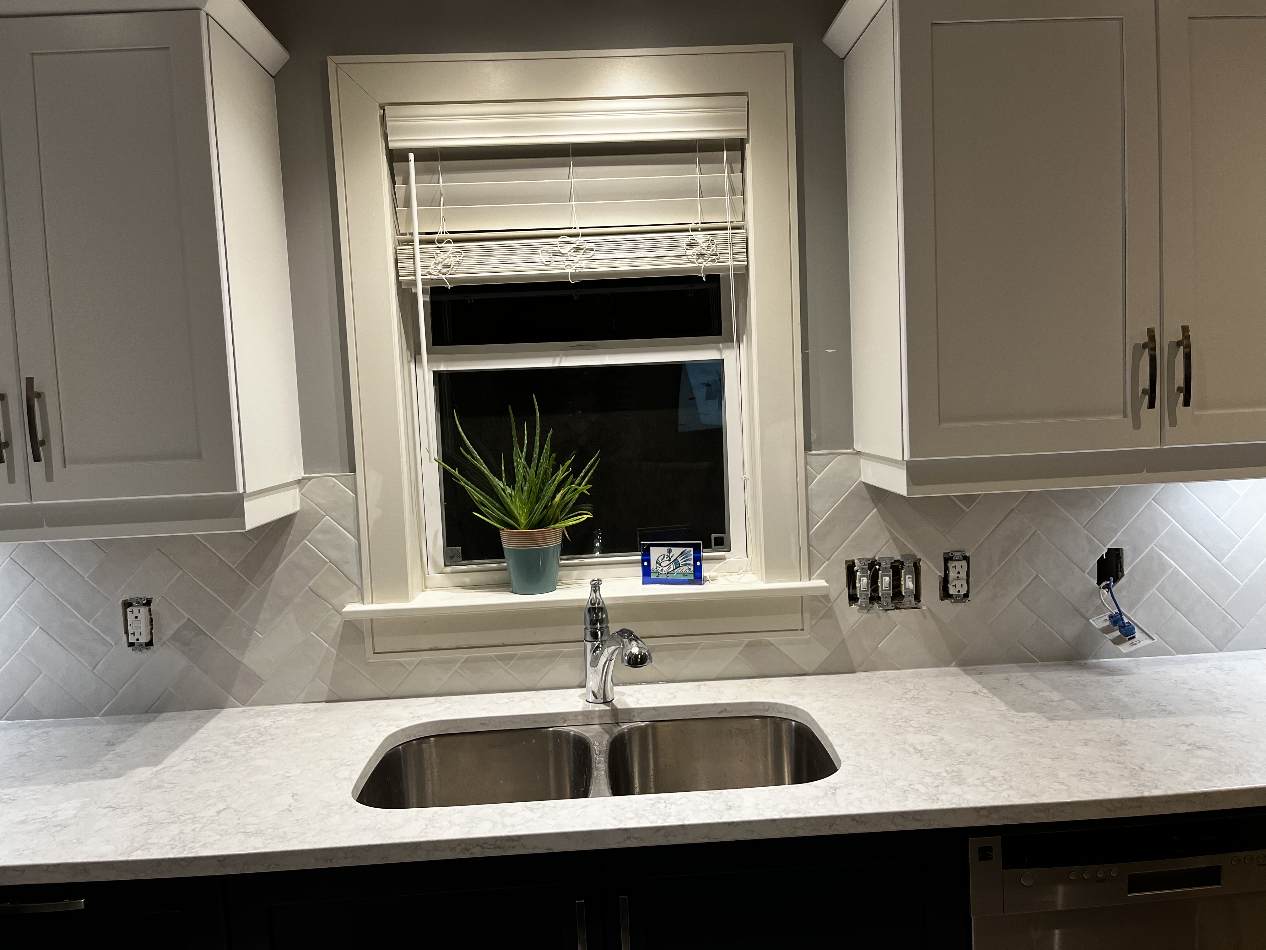 Quartz counters with an undermount sink and white upper cabinet doors finished beautifully with a herringbone tile backsplash