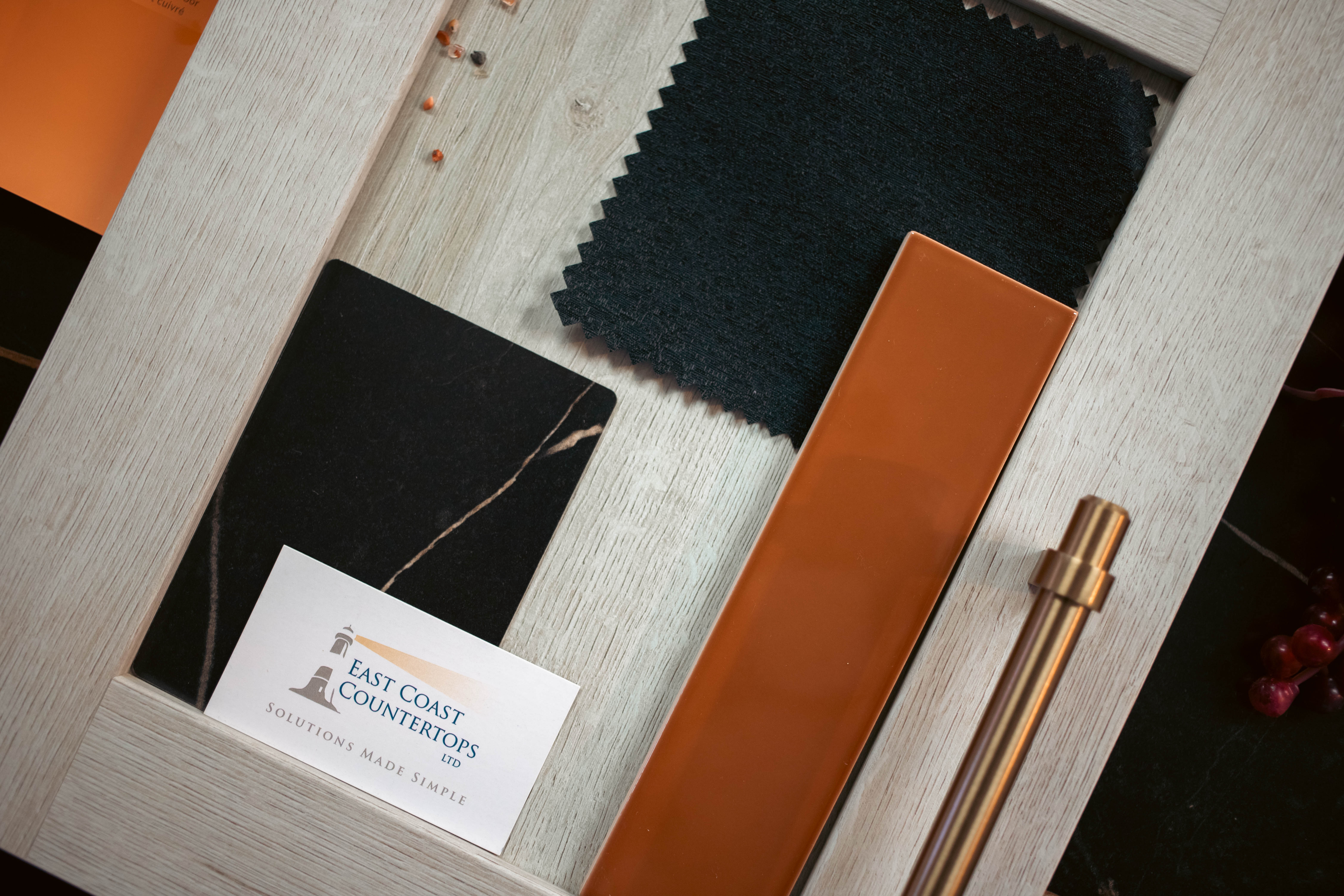 White wooden cabinet door close up with black fabric swatch for blinds, Sahara Noir sample chip and terra shade tile with a brass cabinet door knob